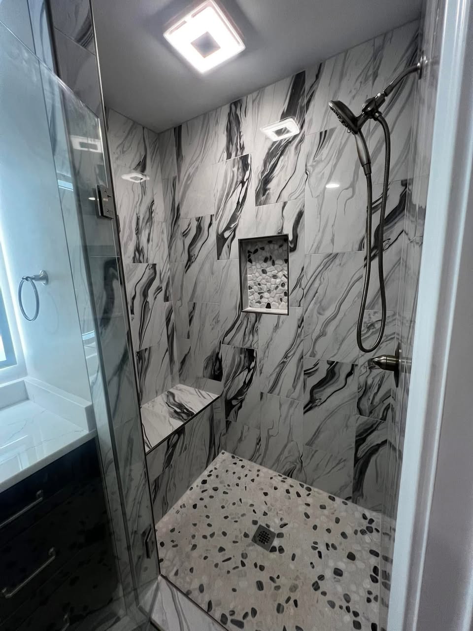 Marble-tile bathroom remodel with built-in seat and shower niche by Crockett Construction