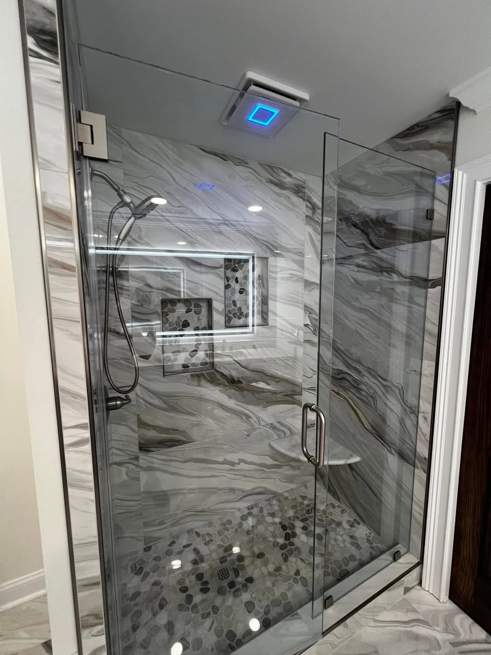 Custom marble-tile shower with glass enclosure and pebble floor by Crockett Construction